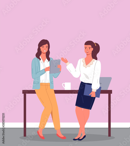 Two employees, colleagues or business women standing leaning on brown desk. Project discussion, business meeting, coffee break. Pink walls, laptop on the table. Office interior. Flat vector image