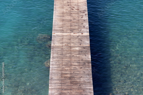 Empty wooden pier with wet footprints in azure sea with clear water, top view. Beach vacation, swimming concept © Oleg