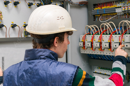 An electrician in an engineering helmet opens the switch box. The technician works in the electrical control room. Service of power distribution switchboards. photo
