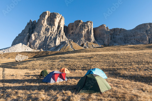 Camping in nature. Tents on meadow. Autumnal scenery in highlands. Alpine landscape circled by colorful yellow and red fall trees in Dolomite mountains, Southern Tyrol area. Dolomites, Italy Europe