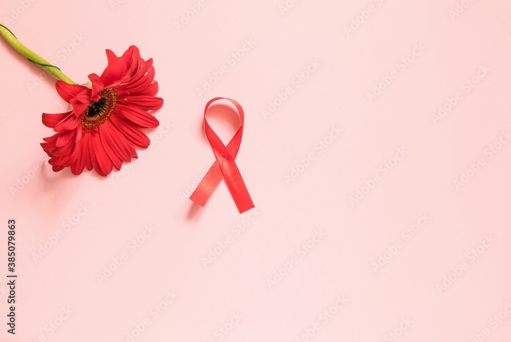 Red ribbon with a red gerbera flower on a pink background. The concept of medicine and human health care. World breast cancer awareness and prevention day. Red ribbon with a red gerbera flower on a pink background. The concept of medicine and human health care. World breast cancer awareness and prevention day.
