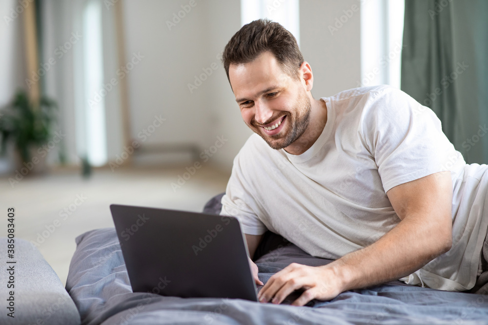 Happy Freelancer Man Using Laptop Working Online Lying In Bed Happy Freelancer Man Using Laptop Working Online Lying In Bed