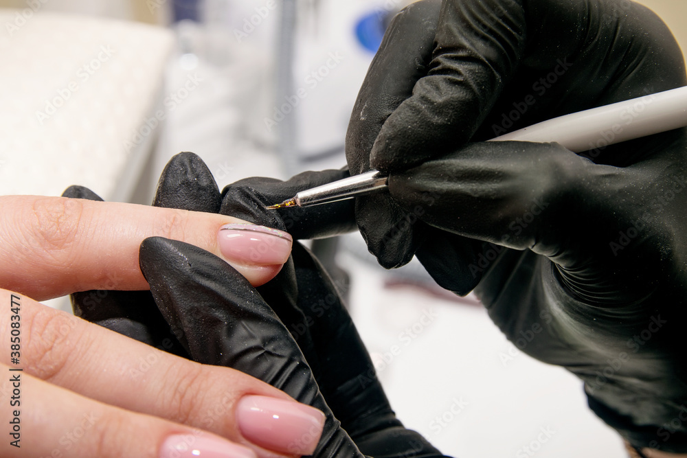 Close-up shot of a manicurist in black gloves applying a pattern with a brush to nails