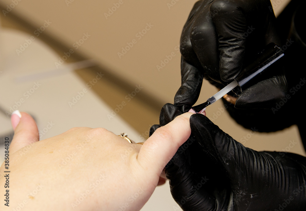 Close-up shot of a manicurist in black gloves applying gel polish on nails