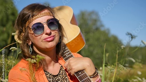 Slow motion. nature, summer vacation, vacation and people concept - happy smiling woman in sunglasses stands with a guitar on her shoulder. photo