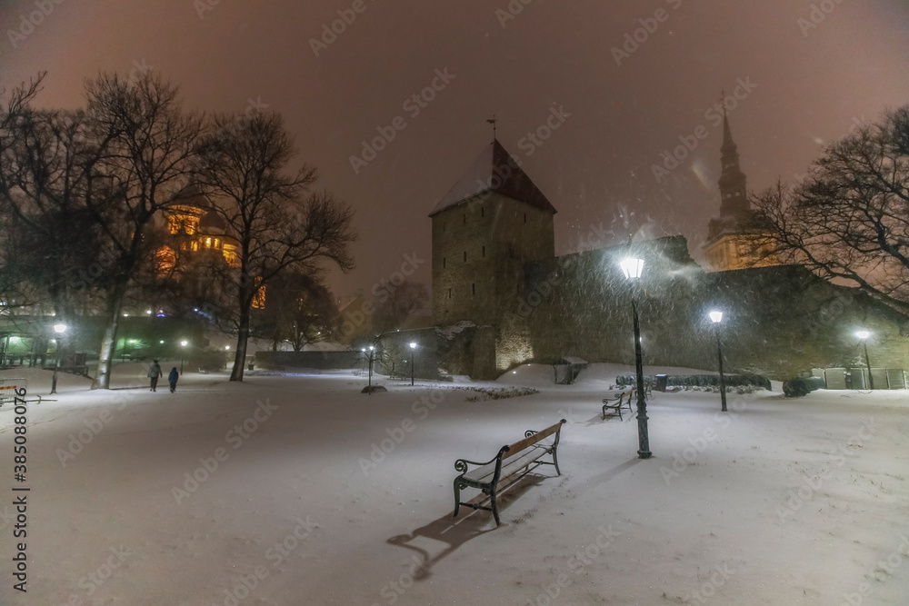 Winter night scene with the heavy snowfall of the historic Tallinn town wall,its defensive towers and illuminated churches in the background Winter night scene with the heavy snowfall of the historic Tallinn town wall,its defensive towers and illuminated churches in the background
