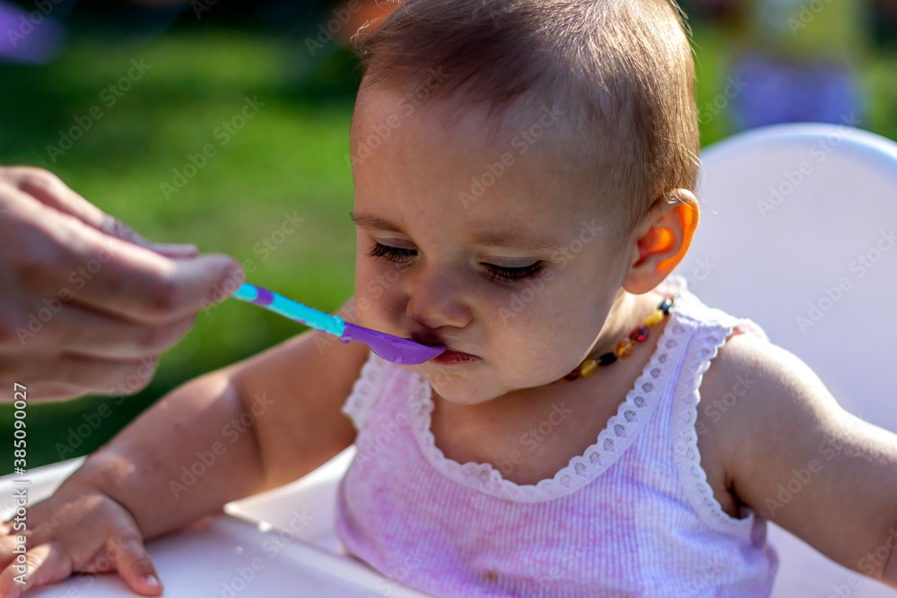 Photo of a mother feeds the daughter outdoors. Mother feeding her cute baby daughter while enjoying in park. Cute little girl eating lunch from her mom hand. Cute Caucasian girl eating food in nature Photo of a mother feeds the daughter outdoors. Mother feeding her cute baby daughter while enjoying in park. Cute little girl eating lunch from her mom hand. Cute Caucasian girl eating food in nature