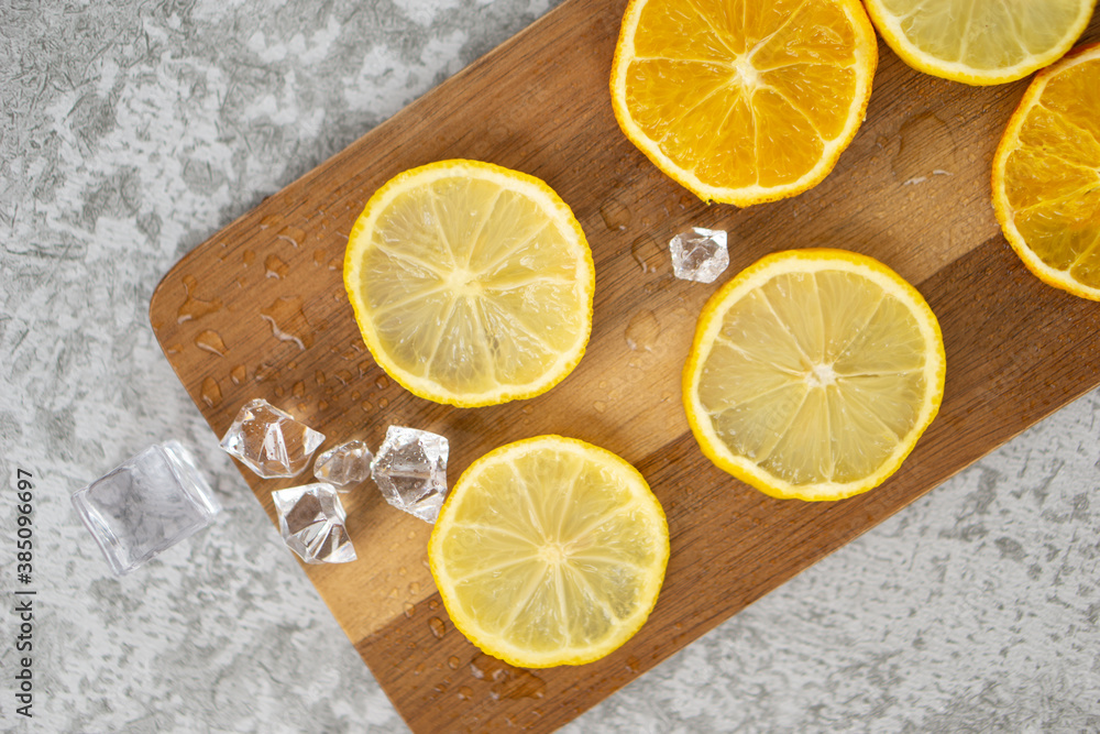 Primer plano de rodajas de limón y naranja sobre una tabla de madera con hielo sobre un fondo gris con textura Primer plano de rodajas de limón y naranja sobre una tabla de madera con hielo sobre un fondo gris con textura