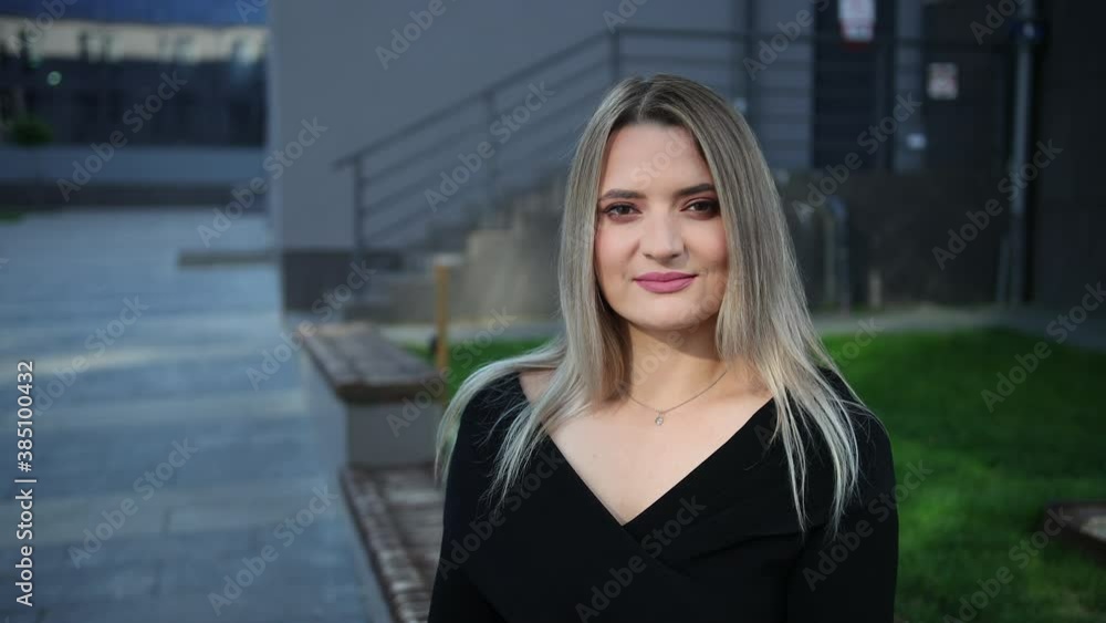 Portrait of a beautiful businesswoman who talks to half-conversationalist and smiles. Behind business buildings, offices Portrait of a beautiful businesswoman who talks to half-conversationalist and smiles. Behind business buildings, offices