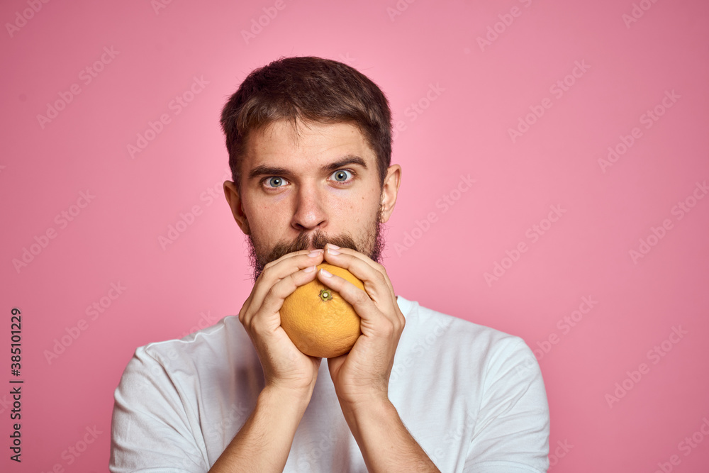 Young man with orange on a pink background in a white t-shirt emotions fun gesticulating with model hands Young man with orange on a pink background in a white t-shirt emotions fun gesticulating with model hands