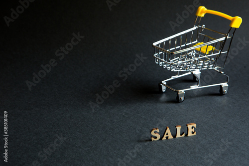 Shopping cart and the inscription "Sale" on a black background. Black Friday, discounts, sale, shopping, interest sign. Space for text