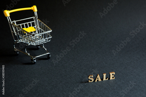 Shopping cart and the inscription "Sale" on a black background. Black Friday, discounts, sale, shopping, interest sign. Space for text