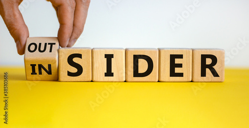 Hand turns a cube and changes the expression 'insider' to 'outsider' or vice versa. Beautiful yellow table, white background.  Copy space. photo
