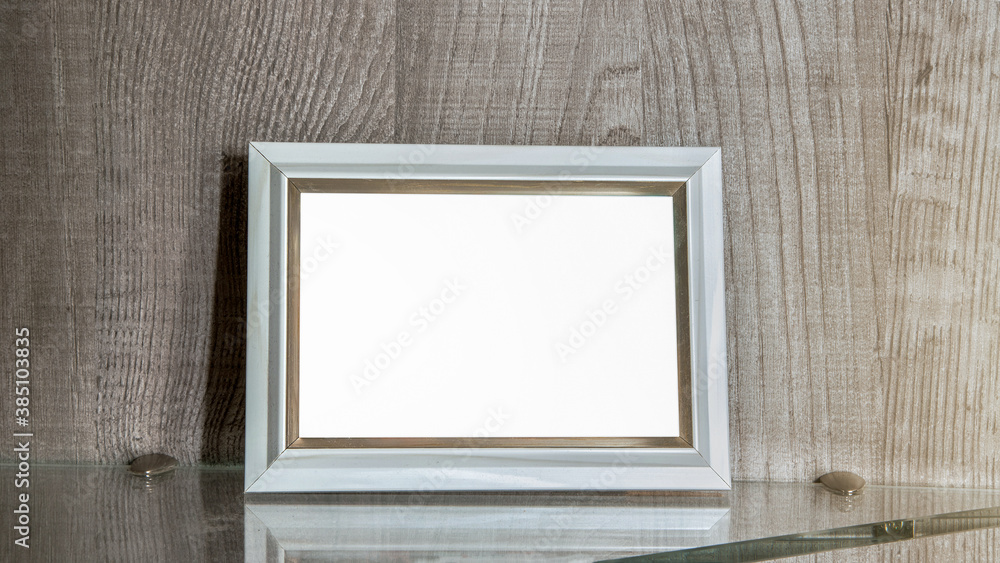 horizontal empty white photo frame with space for mock up stands on glass shelf in living room horizontal empty white photo frame with space for mock up stands on glass shelf in living room