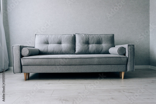 Modern grey sofa with wooden legs in the room