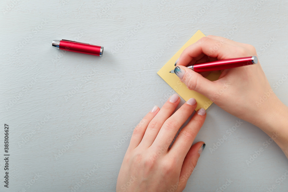 Female hands with fir-tree forest manicure holding red pen over yellow paper stickers. Christmas or winter nail art. Hands care, fingernails design, beauty and health concept. Copy space. Female hands with fir-tree forest manicure holding red pen over yellow paper stickers. Christmas or winter nail art. Hands care, fingernails design, beauty and health concept. Copy space.