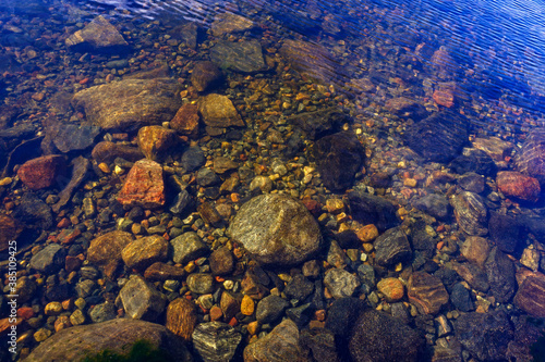 Stones at the bottom of a clear lake with clear water with a blue sky reflection.