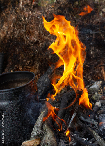 Tourist kettle, kettle in the fire of a burning campfire in a camping trip. Cooking food in the forest on wooden wood during the hike. Active rest and entertainment in nature.