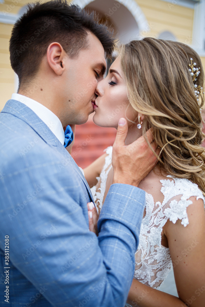 Young stylish guy in the costume of the groom and the bride beautiful girl in a white dress with a train walking on the background of a large house with columns on their wedding day Young stylish guy in the costume of the groom and the bride beautiful girl in a white dress with a train walking on the background of a large house with columns on their wedding day