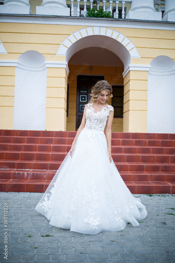 beautiful girl bride in a white dress with a train walking on the background of a large house with columns on their wedding day