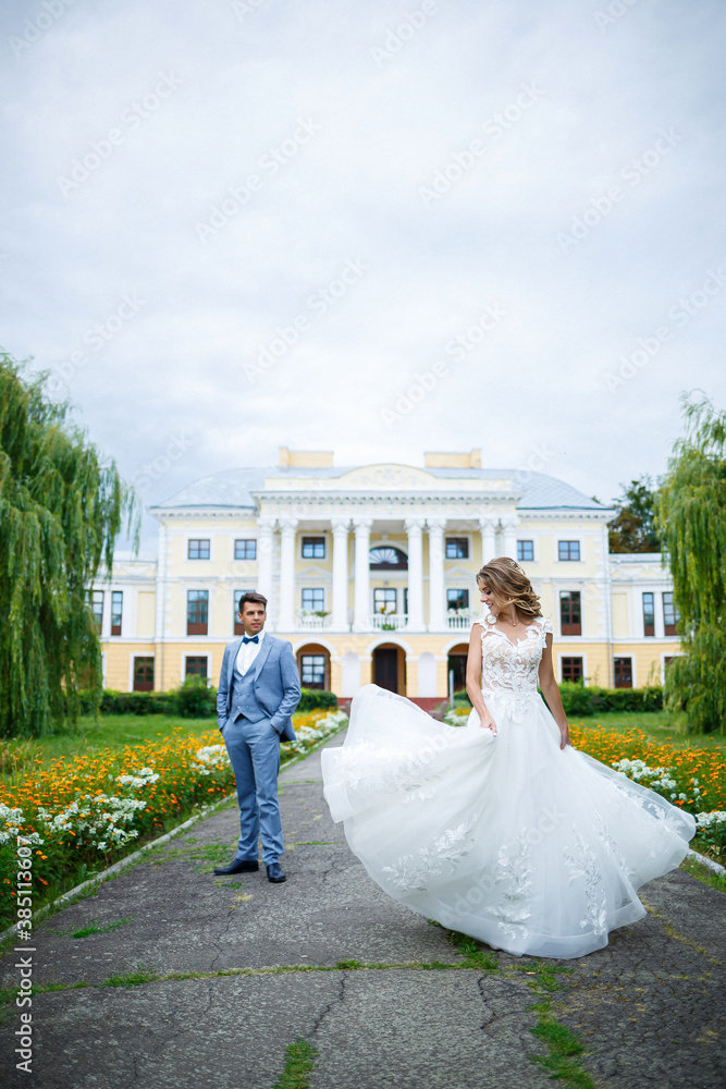 Young stylish guy in the costume of the groom and the bride beautiful girl in a white dress with a train walk in the park on their wedding day Young stylish guy in the costume of the groom and the bride beautiful girl in a white dress with a train walk in the park on their wedding day