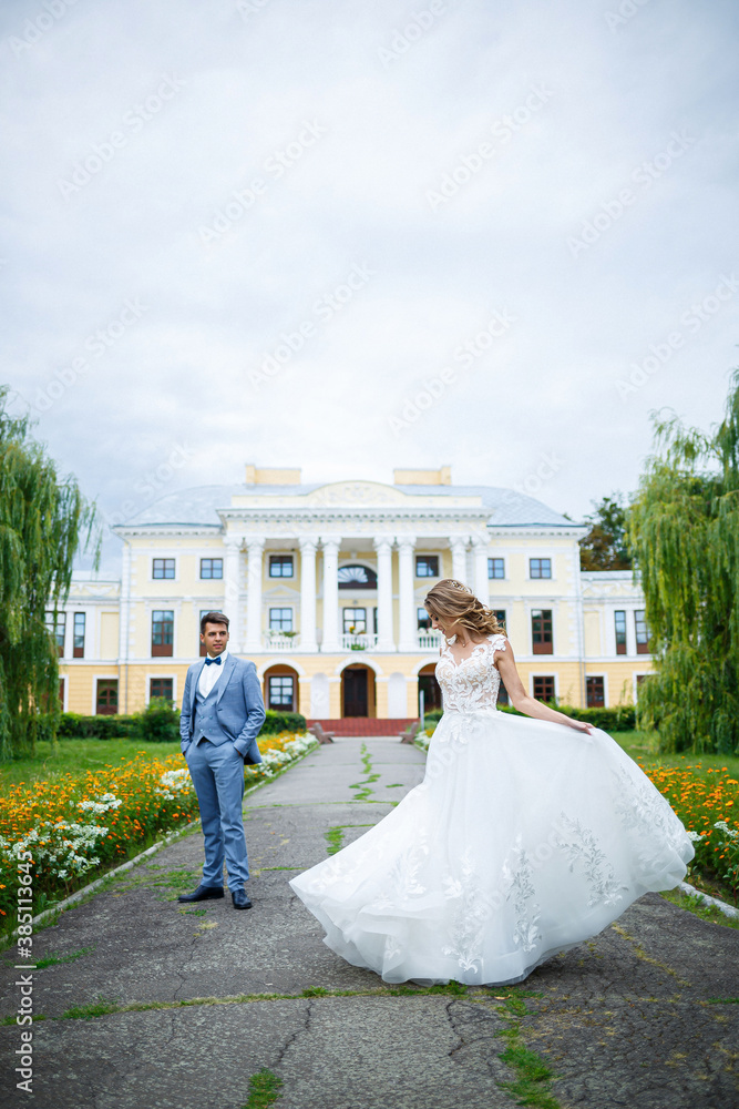 Young stylish guy in the costume of the groom and the bride beautiful girl in a white dress with a train walk in the park on their wedding day Young stylish guy in the costume of the groom and the bride beautiful girl in a white dress with a train walk in the park on their wedding day