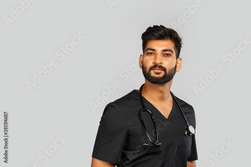 young indian male doctor or surgeon with stethoscope on gray background © Nana_studio