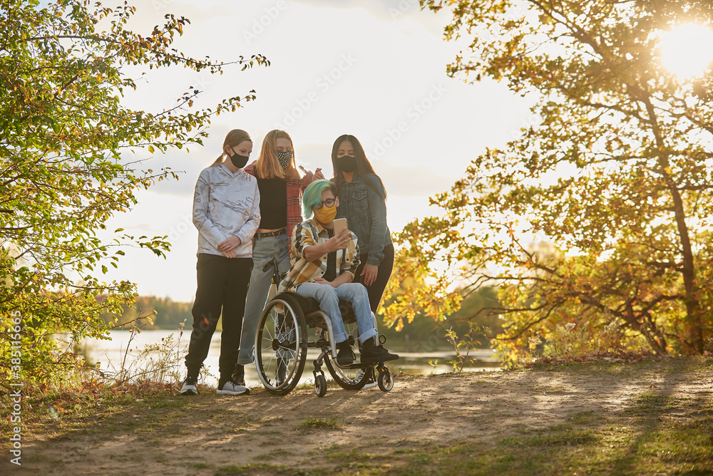 Disabled teen in a wheelchair with multi ethnic group of friends wearing facial masks due to cover-19 pandemic taking a group selfie. Disabled teen in a wheelchair with multi ethnic group of friends wearing facial masks due to cover-19 pandemic taking a group selfie.