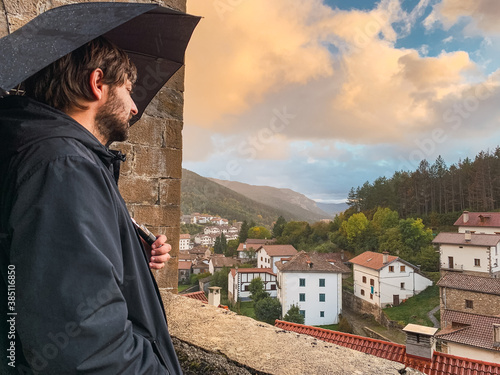 Man with an umbrella looking down on a small town on the mountains