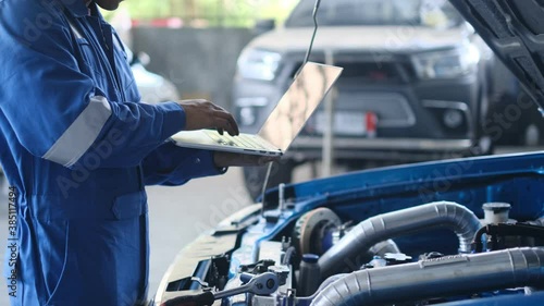 Mechanic Asian man using laptop computer examining tuning fixing repairing car engine automobile vehicle parts using tools equipment in workshop garage support and service in overall work uniform