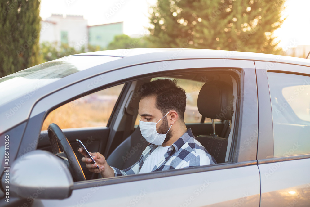 Man wearing a mask, press the mobile phone on the car. A man looking at the phone while driving.