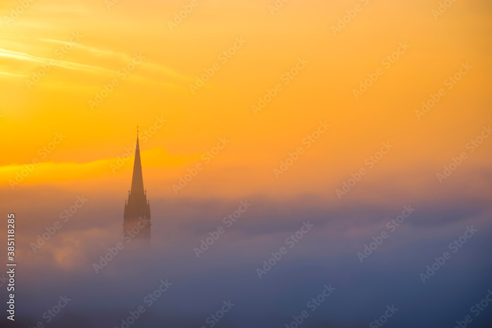 Fototapeta premium Church of the Sacred Heart of Jesus surrounded by fog and clouds, in Graz, Styria region, Austria, at sunrise. Beautiful foggy morning over the city of Graz, in autumn