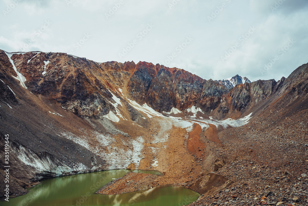 Beautiful glacial lake of acid green color. Amazing emerald highland lake near glacier and sharp mountain top. Pointy rocks under cloudy sky. Awesome alpine landscape with lake of unusual green tones.