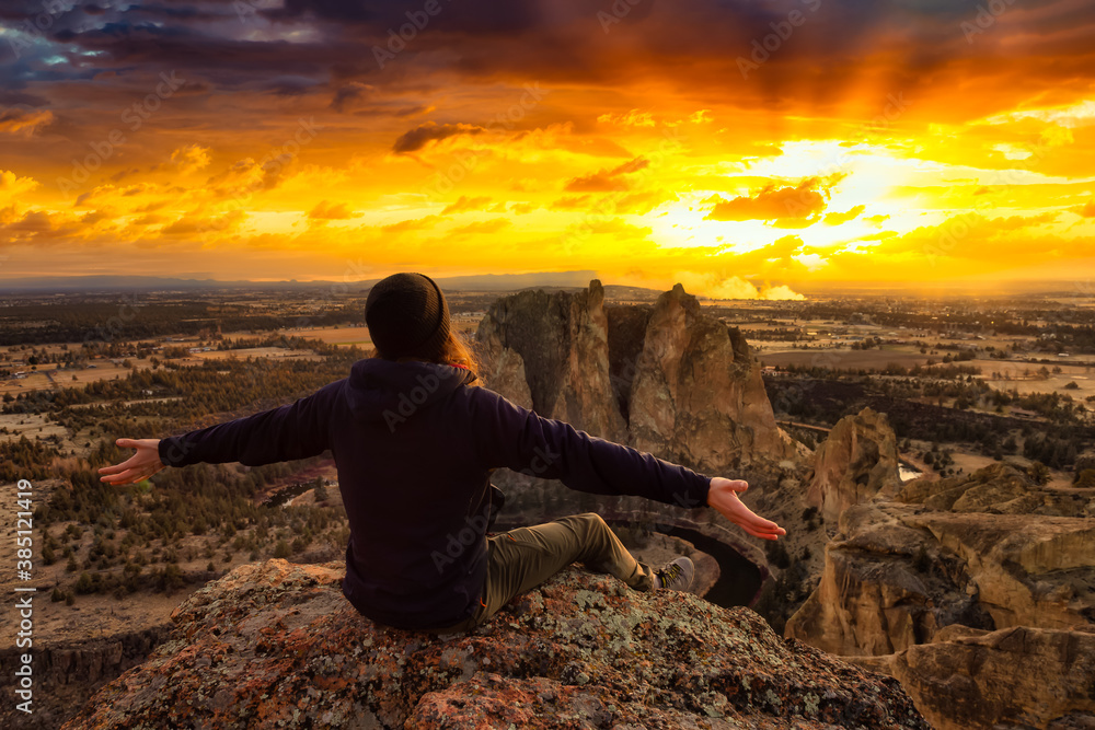 Obraz premium Man enjoying the Beautiful American Mountain Landscape. Arms Open. Taken in Smith Rock, Redmond, Oregon, America. Dramatic Sunset Artistic Render. Concept: Adventure, Holiday and Travel