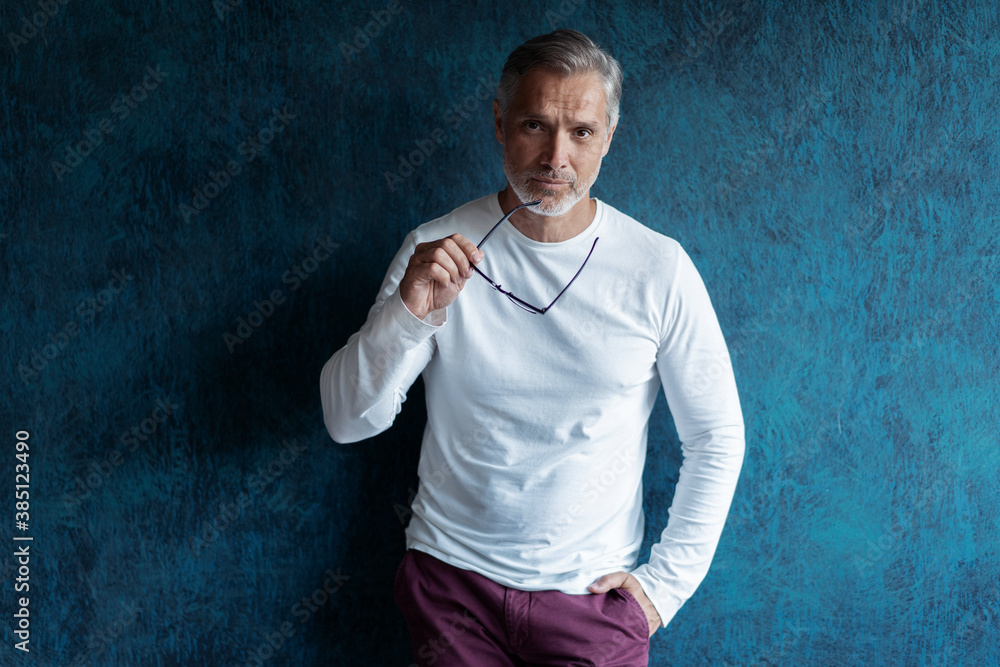 Casual Grey-haired Mature handsome man portrait over dark blue wall background Casual Grey-haired Mature handsome man portrait over dark blue wall background