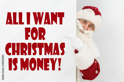 Santa Claus points his fingers at the board with the text - ALL I WANT FOR CHRISTMAS IS MONEY