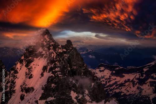 Beautiful aerial landscape view of the snow covered mountains with glowing clouds from the sunlight during sunset. Picture taken from an airplane near Squamish, North of Vancouver, BC, Canada.