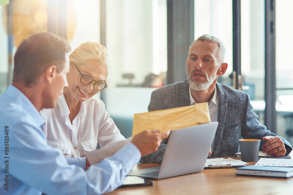 Office life. Mature business people discussing something and smiling while working together in the modern office or coworking space Office life. Mature business people discussing something and smiling while working together in the modern office or coworking space