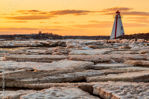 Frozen sea with large ice blocks sheets against a red and white lighthouse during sunset in Charlottetown Prince Edward Island, Canada