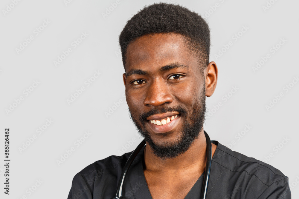 Fototapeta premium close-up portrait of a happy African doctor in black medical uniform on a gray background.