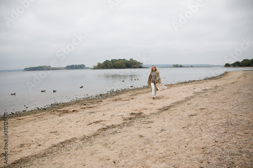 A young girl walks along the beach. Blonde girl walks in the Park near the lake
