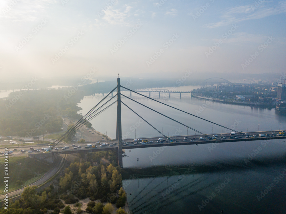Obraz premium Aerial drone view. North bridge in Kiev in the rays of a sunny morning. Autumn haze in the air, cars are driving across the bridge.