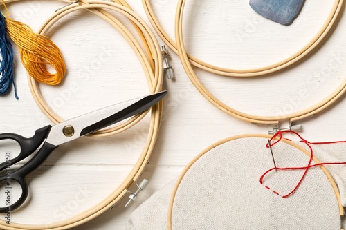 Round stitching or embroidery frame with red stitching and sewing tools on white wooden table