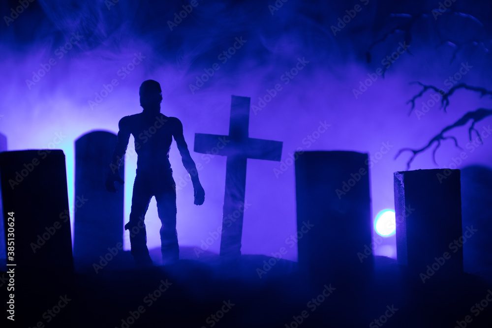 Fototapeta premium Scary view of zombies at cemetery dead tree, moon, church and spooky cloudy sky with fog, Horror Halloween concept with glowing pumpkin. Selective focus