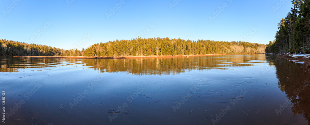 Calming panoramic reflection of clear skies and a forested hill in Strathgartney Provincial Park, Prince Edward Island, Canada