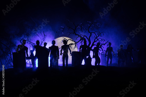 Scary view of zombies at cemetery dead tree, moon, church and spooky cloudy sky with fog, Horror Halloween concept with glowing pumpkin. Selective focus