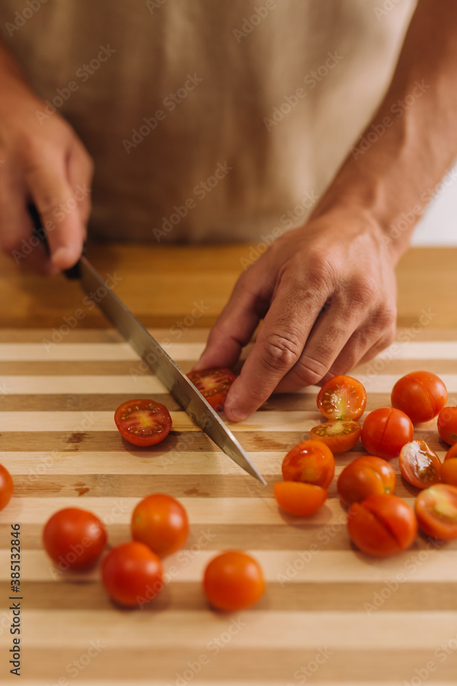 Male hands slicing cherry tomatoes on a cooking board. Male hands slicing cherry tomatoes on a cooking board.