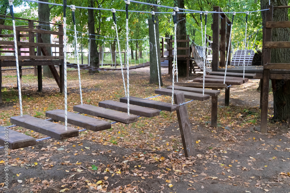 The bridge of logs tied to the ropes. lonely Broken bridge. Close up. Without children. Autumn park. Painted wooden plank. rope Park for kids in the green forest. The bridge of logs tied to the ropes. lonely Broken bridge. Close up. Without children. Autumn park. Painted wooden plank. rope Park for kids in the green forest.
