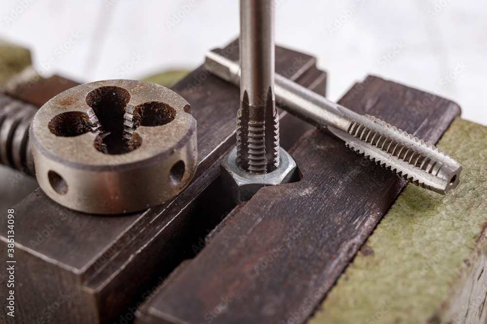 Threading a metal nut in a vice. Minor locksmith work in the workshop. Threading a metal nut in a vice. Minor locksmith work in the workshop.