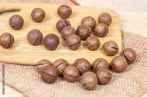 Brown macadamia nuts with wooden cutting board on light textile background.